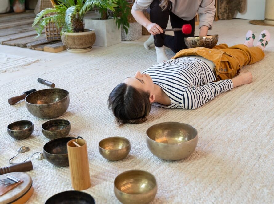 A facilitator leads a woman to an Asian-inspired sound bath using bronze singing bowls and a gong.