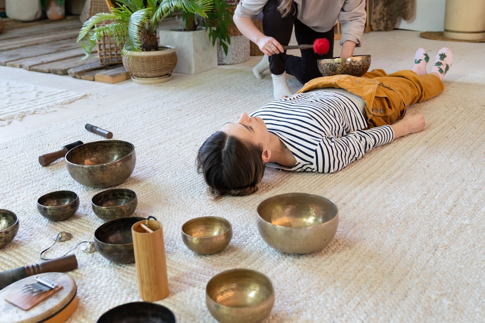 A facilitator leads a woman to an Asian-inspired sound bath using bronze singing bowls and a gong.
