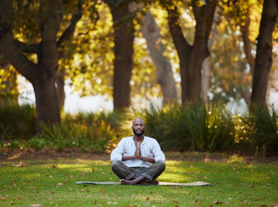 Full-body shot of a young man meditating outdoors in a park.