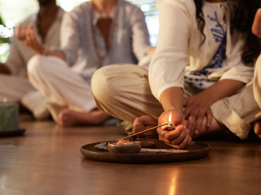 A group of people sitting on the floor posing in a spiritual practice while a woman lights incense.