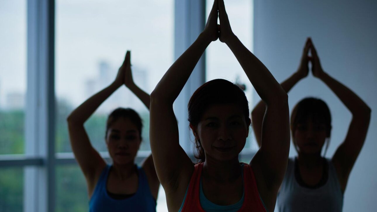 Three yoga practitioners posing with their arms stretched over their heads.